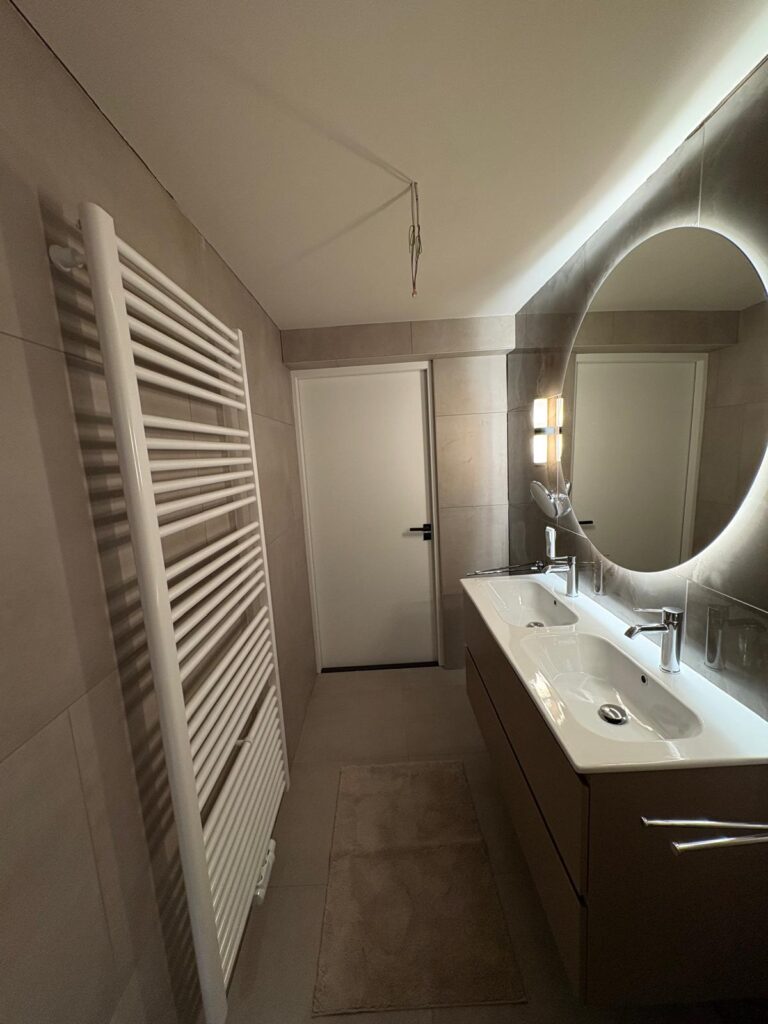 Badkamer met dubbele wastafel, ronde spiegel en handdoekradiator