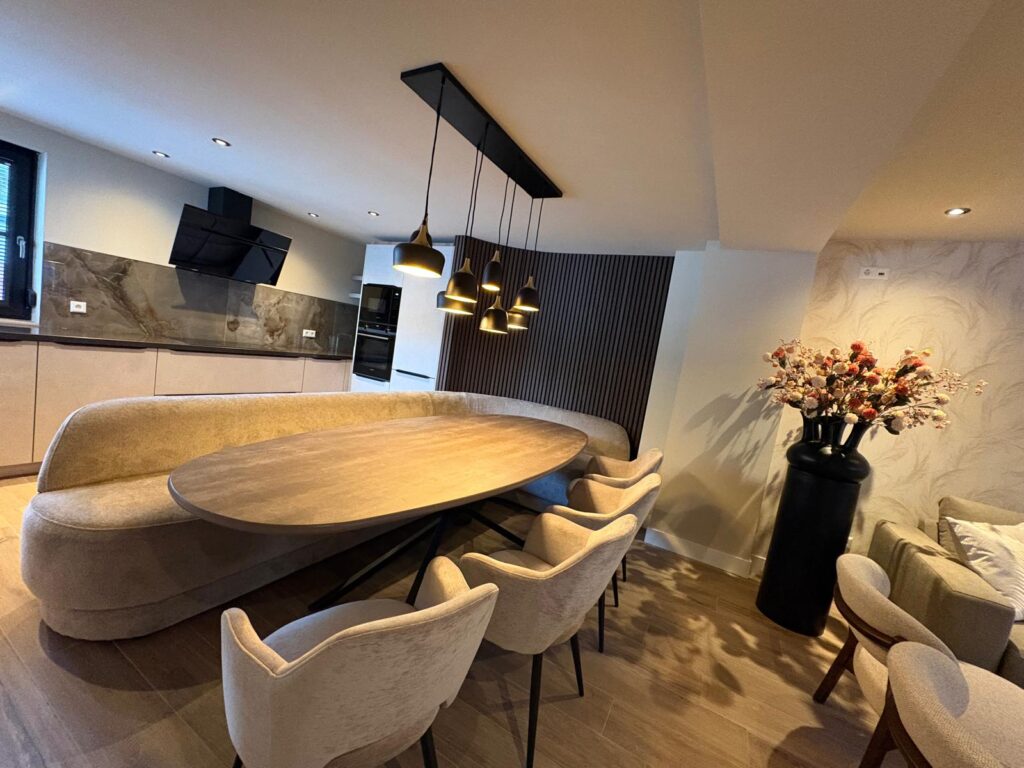 Ovale eettafel met ronde bank onder de hanglampen, met de keuken erachter