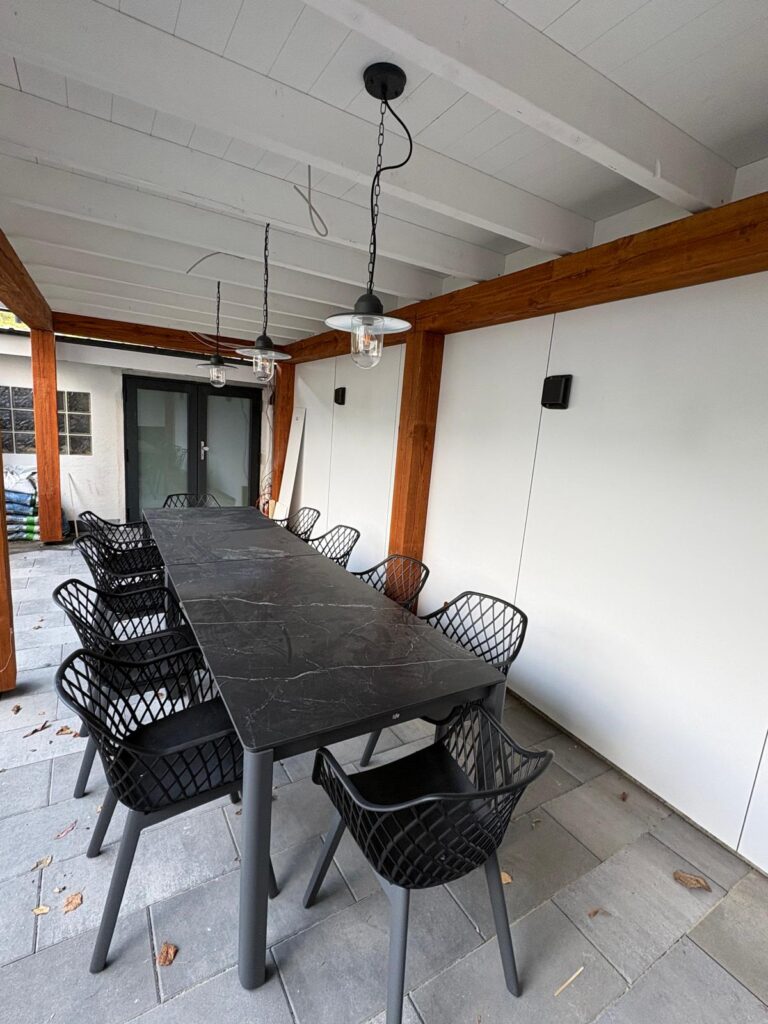 Overdekt terras met lange tafel en zwarte stoelen