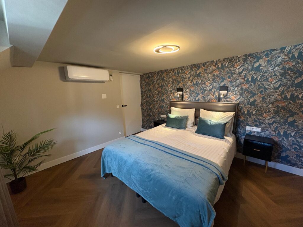 Slaapkamer met tweepersoonsbed, bloemenbehang en airco