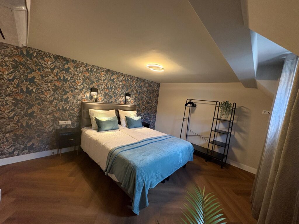 Slaapkamer onder het schuine dak met bloemenbehang en een open kledingrek