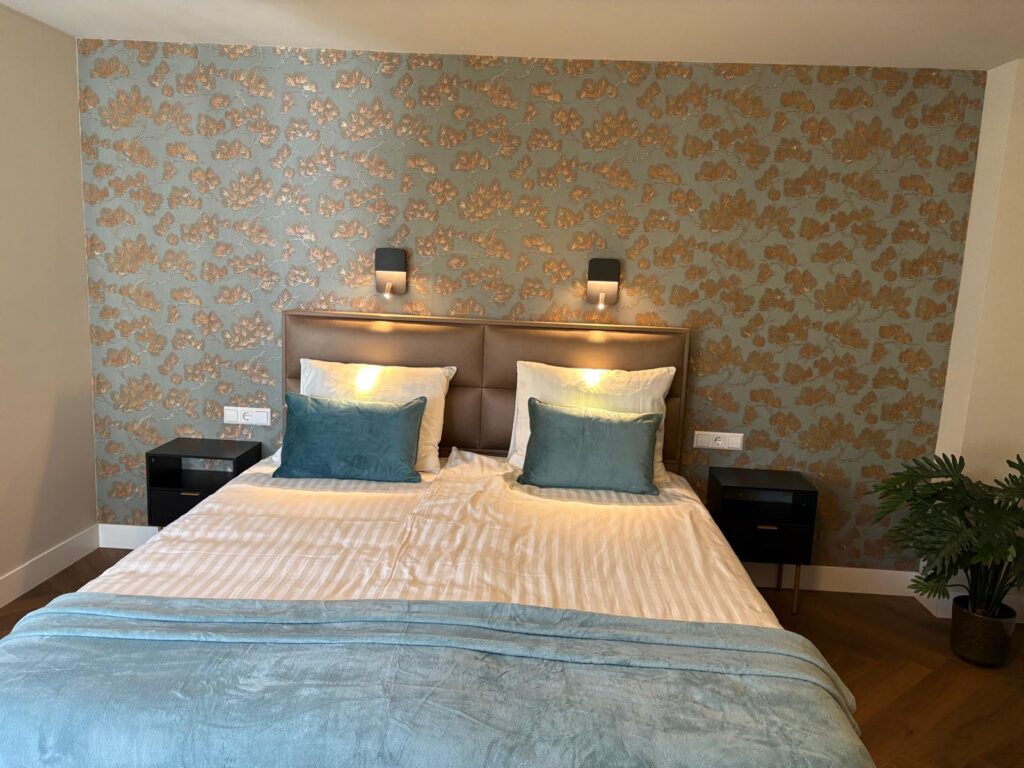 Tweepersoonsbed met blauwgroene kussens tegen behang met gouden bladeren