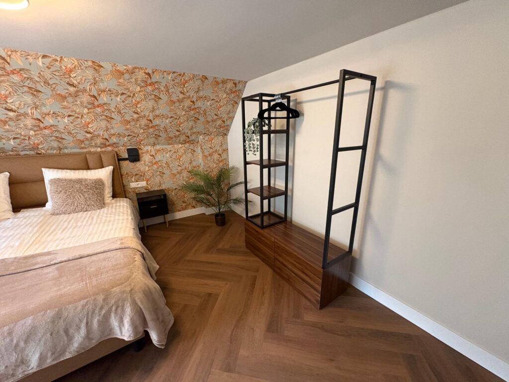 Slaapkamer met tweepersoonsbed, oranje bloemenbehang en een open kledingrek
