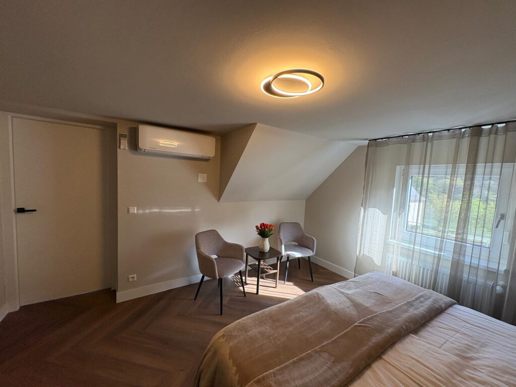Zolderslaapkamer met twee stoelen en een tafeltje bij het raam